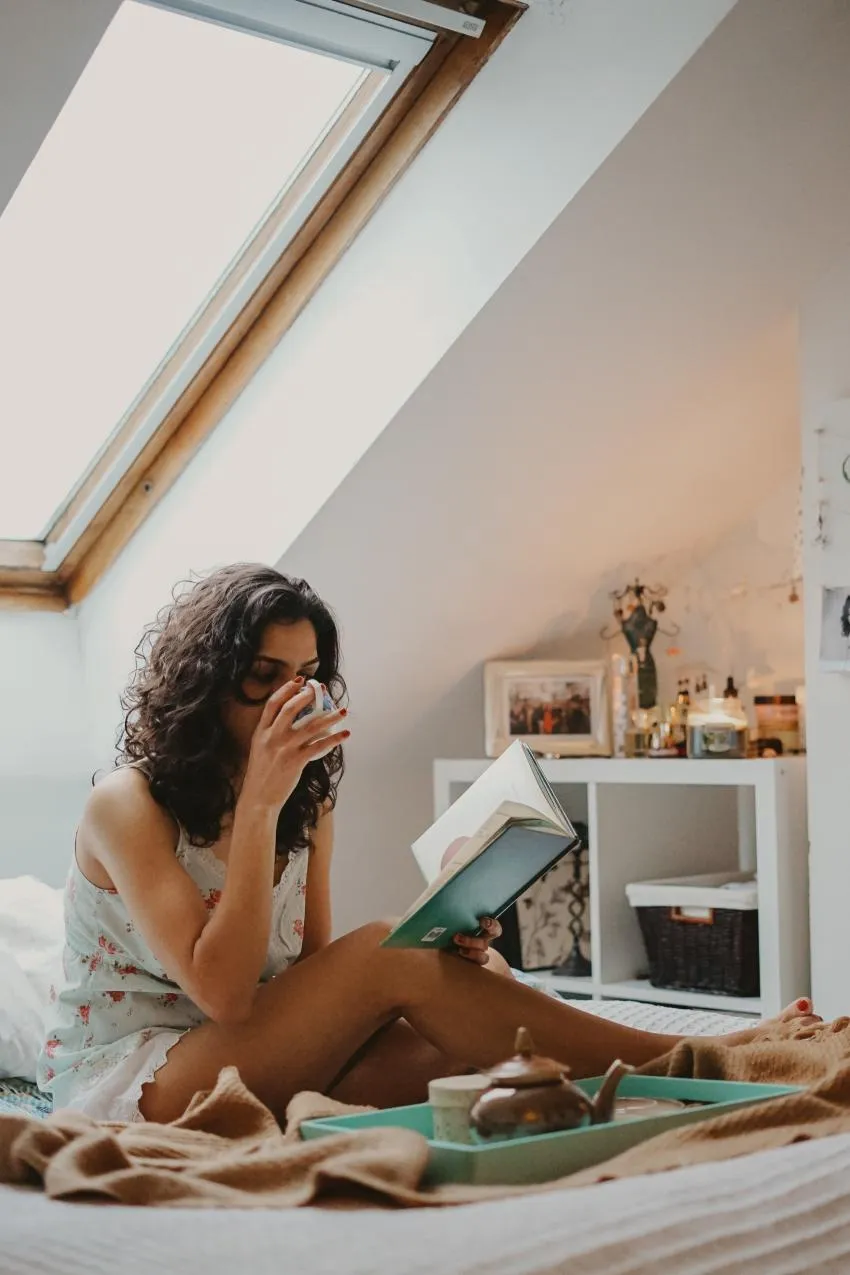Woman drinking tea while reading Invest In Yourself
