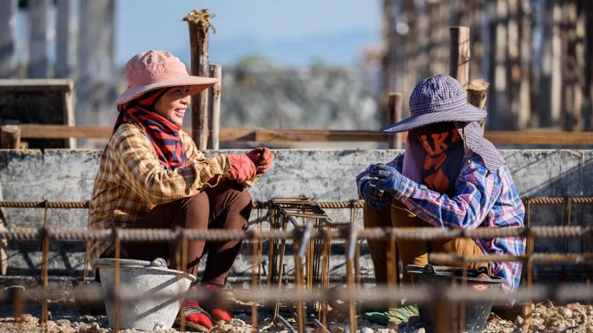 Two women migrant workers talk during the workday, one with facial covering