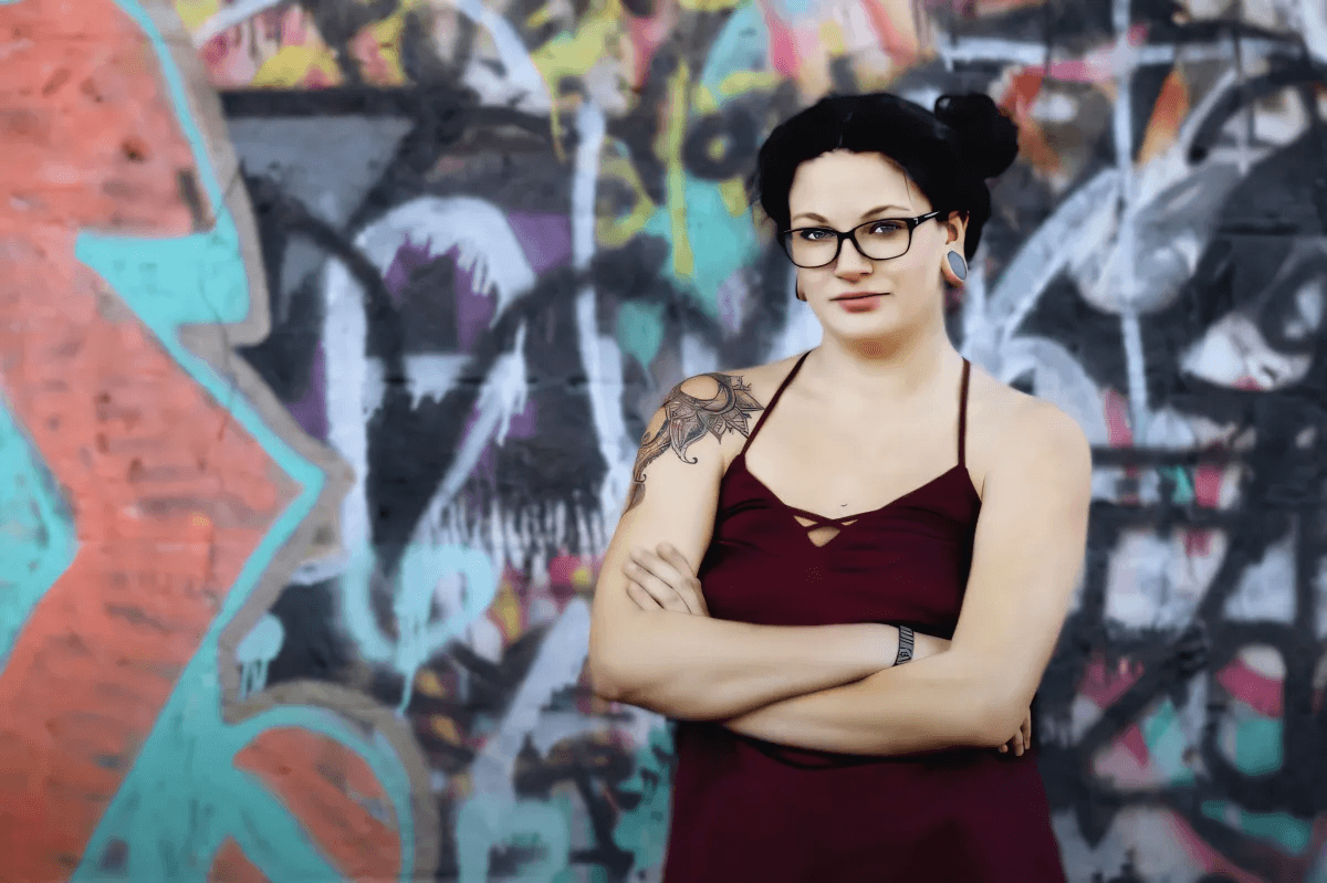 woman with a tattoo and glasses looking confidently into the camera