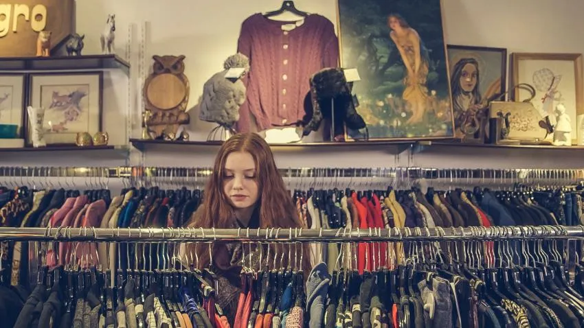 Girl thrift shopping. Racks with clothes. 