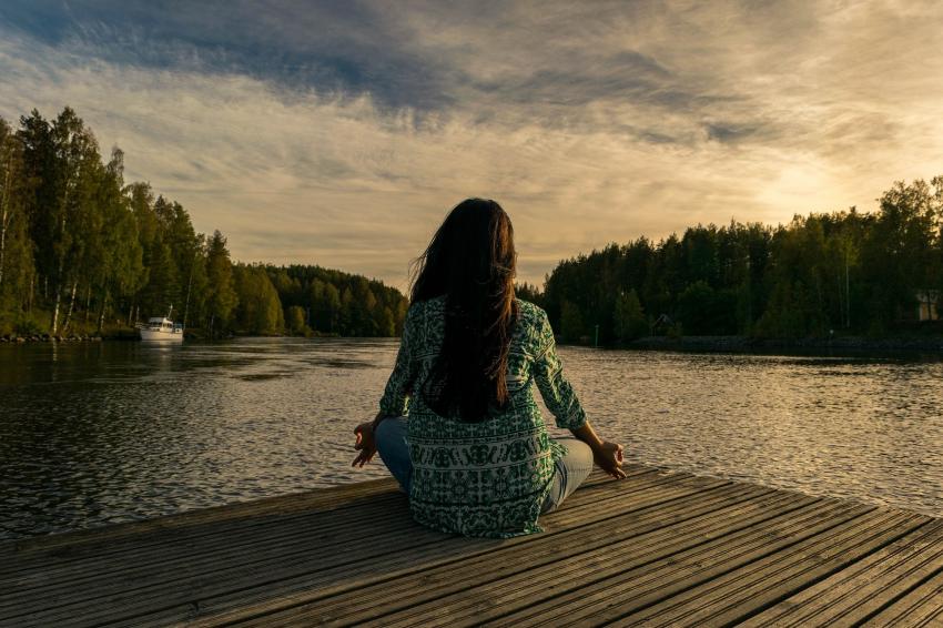 A woman sitting outside on a pier next to a lake doing yoga