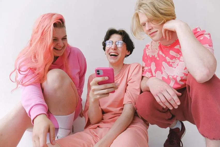 Three people dressed in pink laughing with a pink iphone
