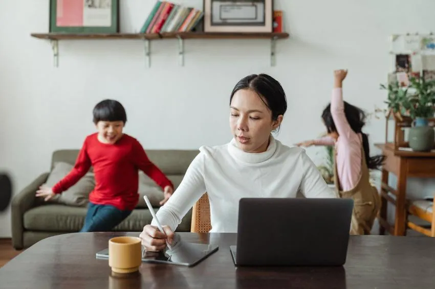 Woman at her computer while kids run in the background